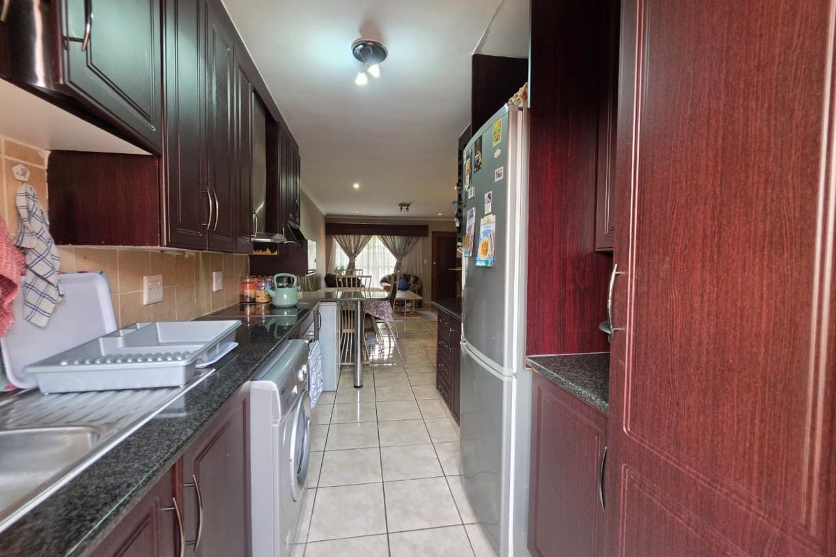 A functional galley-style kitchen featuring dark wood cabinetry, granite countertops, and tiled flooring, leading into an open-plan living area.