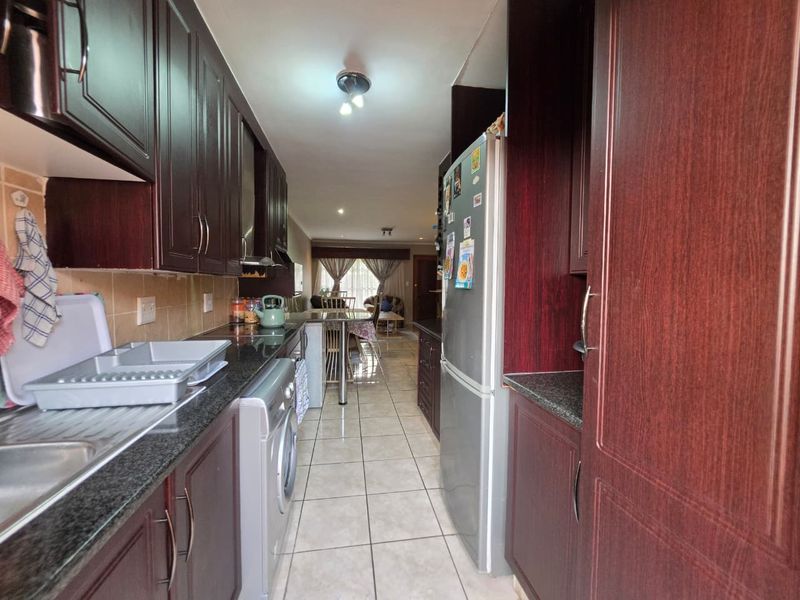 A functional galley-style kitchen featuring dark wood cabinetry, granite countertops, and tiled flooring, leading into an open-plan living area.