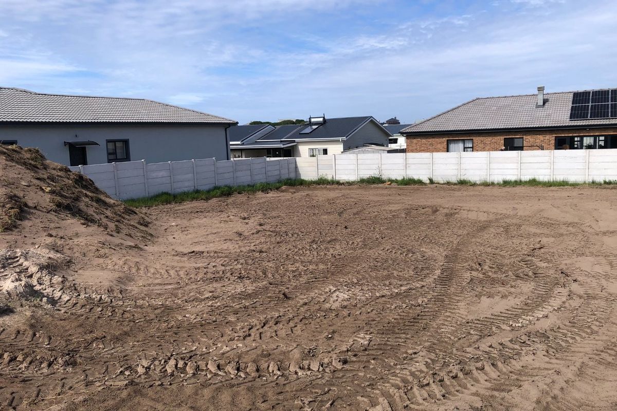 A vacant residential plot featuring cleared sandy ground and a surrounding precast concrete boundary wall in a developed neighborhood.