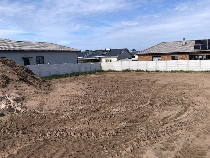 A vacant residential plot featuring cleared sandy ground and a surrounding precast concrete boundary wall in a developed neighborhood.