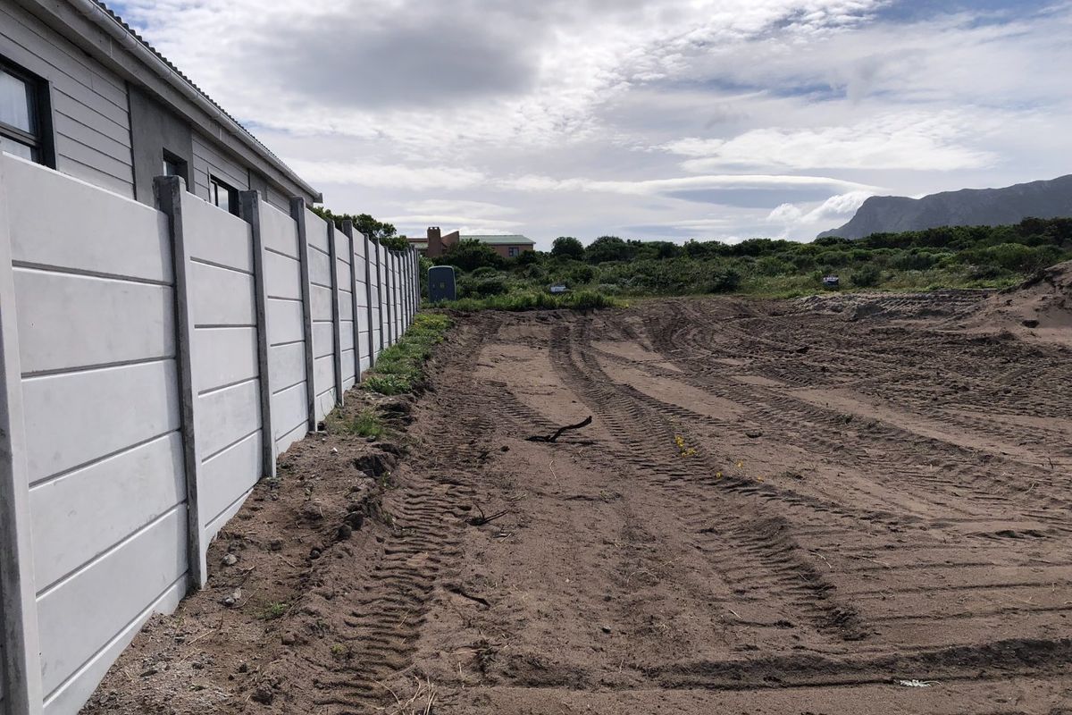 A view of a cleared residential plot featuring a sturdy precast concrete boundary wall and natural landscape surroundings.