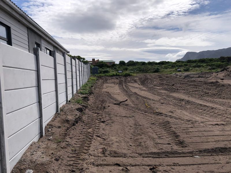 A view of a cleared residential plot featuring a sturdy precast concrete boundary wall and natural landscape surroundings.