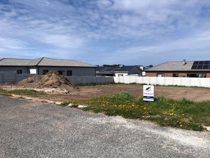 A vacant residential plot featuring a precast concrete boundary wall and gravel road access, ready for development in a established neighborhood.