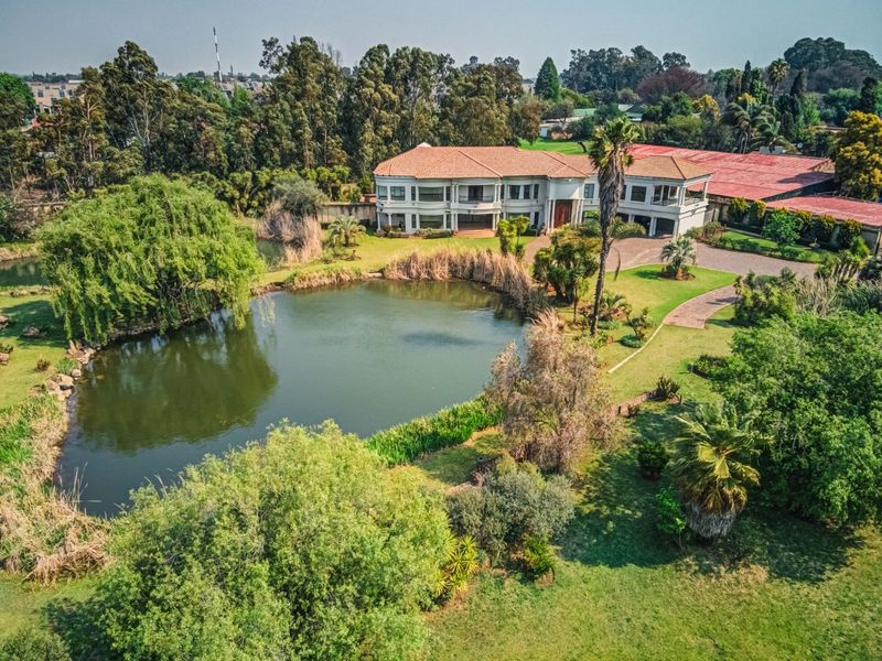 Aerial view of a large residential property featuring a private pond, expansive landscaped gardens, and a multi-level home with a paved driveway.