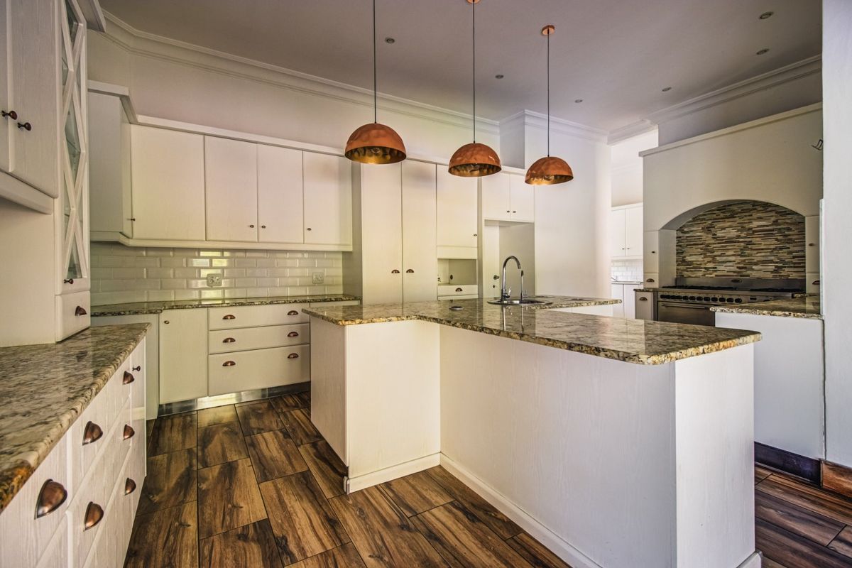 Spacious kitchen featuring granite countertops, a central island, subway tile backsplash, and built-in cooking appliances with modern pendant lighting.
