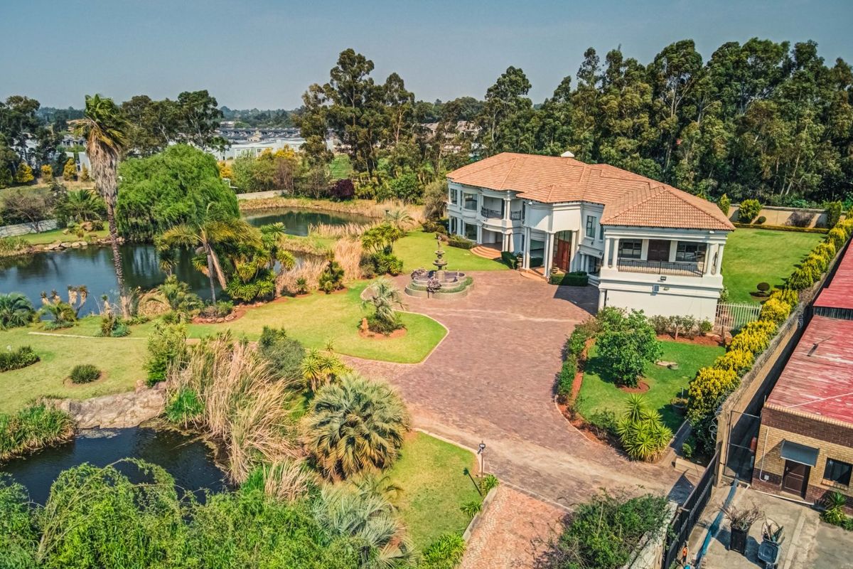 Aerial view of a large luxury residence featuring extensive landscaped gardens, a private pond, paved driveway, and a central water feature.