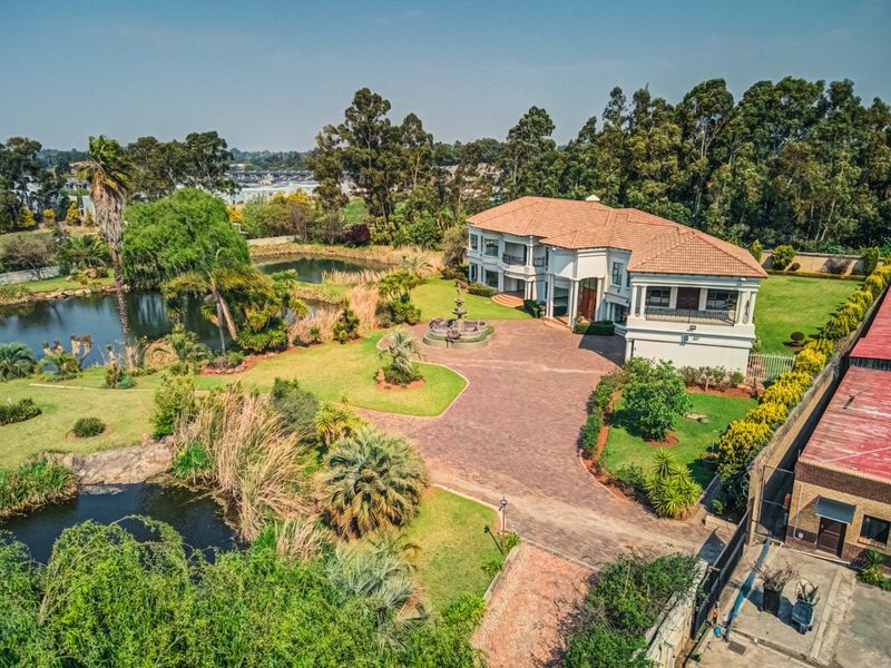 Aerial view of a large luxury residence featuring extensive landscaped gardens, a private pond, paved driveway, and a central water feature.