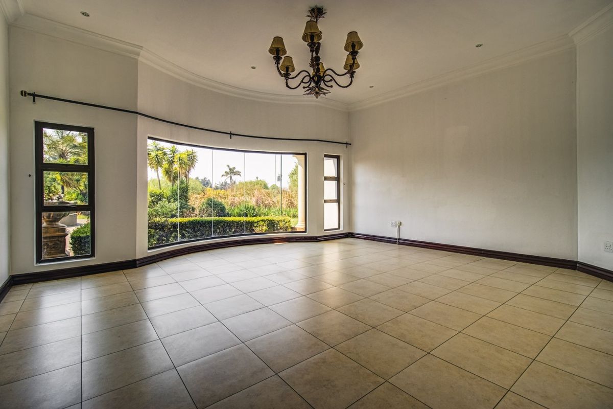 Spacious, light-filled living area featuring large bay windows with garden views, neutral tiled flooring, and elegant chandelier lighting.
