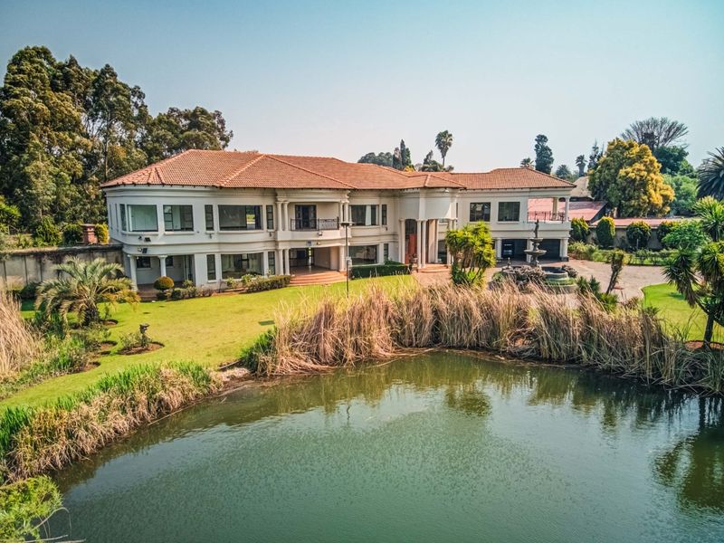 Aerial view of a large, multi-level residential property featuring a terracotta tile roof, expansive landscaped gardens, and a prominent water feature.