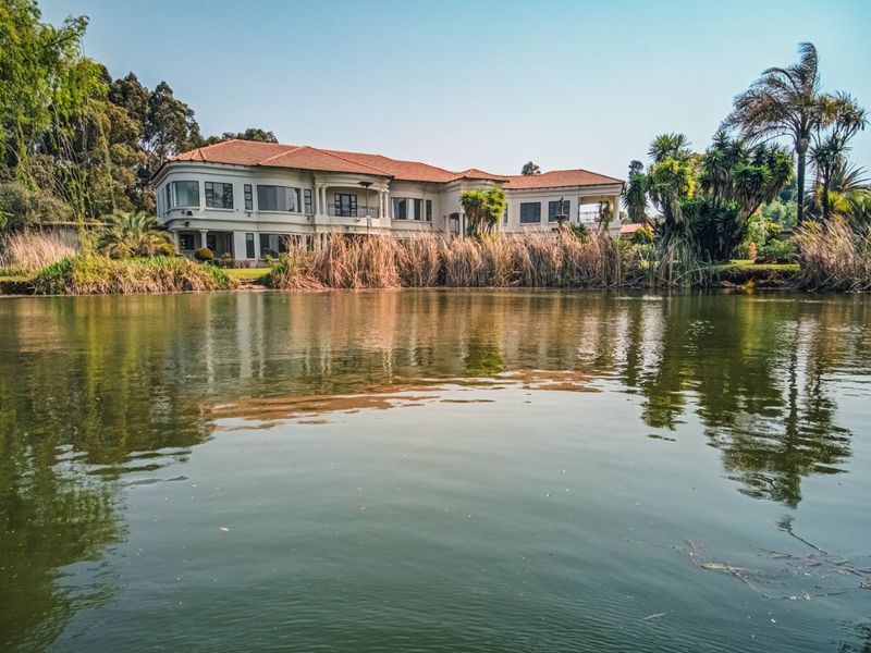 A scenic view of the rear elevation of a large residence featuring a terracotta tile roof, balconies, and expansive windows overlooking a private waterfront.