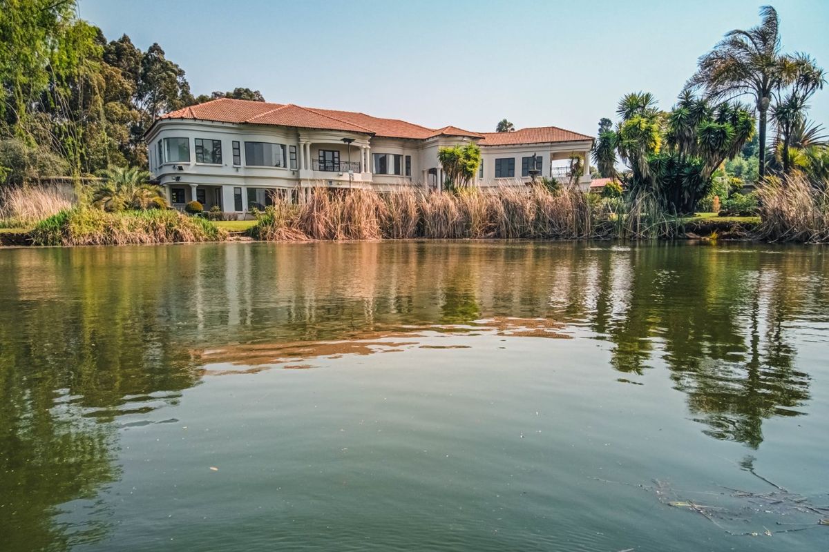 A scenic view of the rear elevation of a large residence featuring a terracotta tile roof, balconies, and expansive windows overlooking a private waterfront.