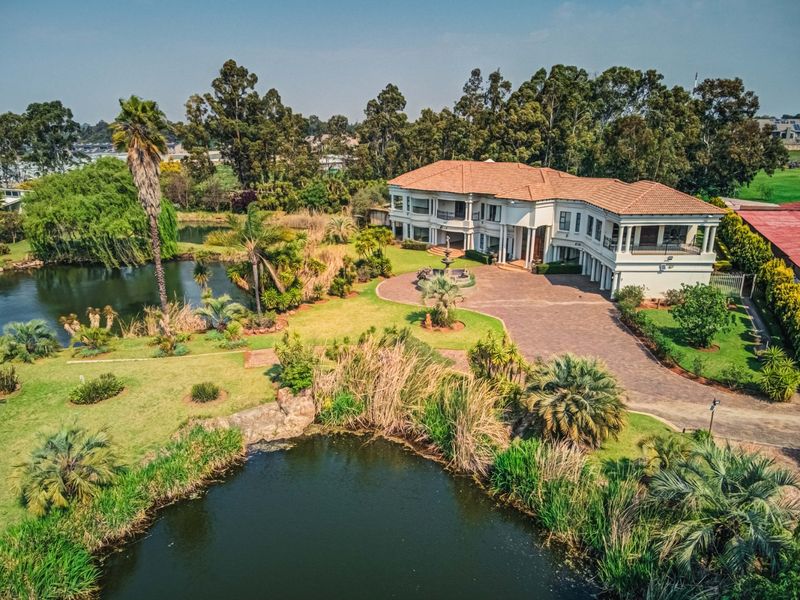 Aerial view of a large multi-level residence featuring a paved driveway, landscaped gardens, and a scenic water feature.