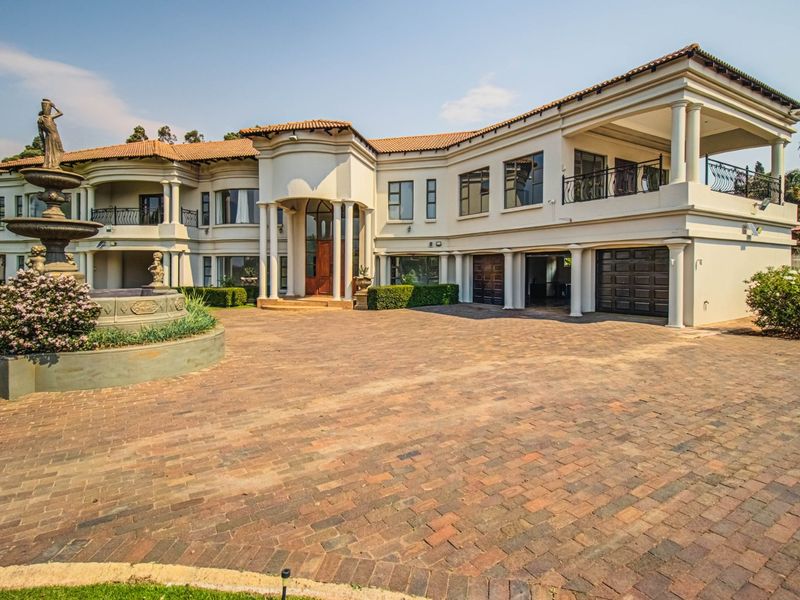 Grand double-story residence featuring a large brick-paved driveway, decorative stone fountain, covered entrance, and upper-level balcony with wrought iron railings.