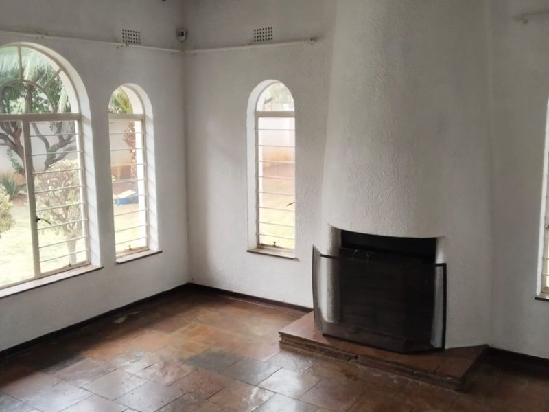 Spacious living room featuring exposed timber ceiling beams, arched windows, and a prominent built-in fireplace with stone tile flooring throughout.