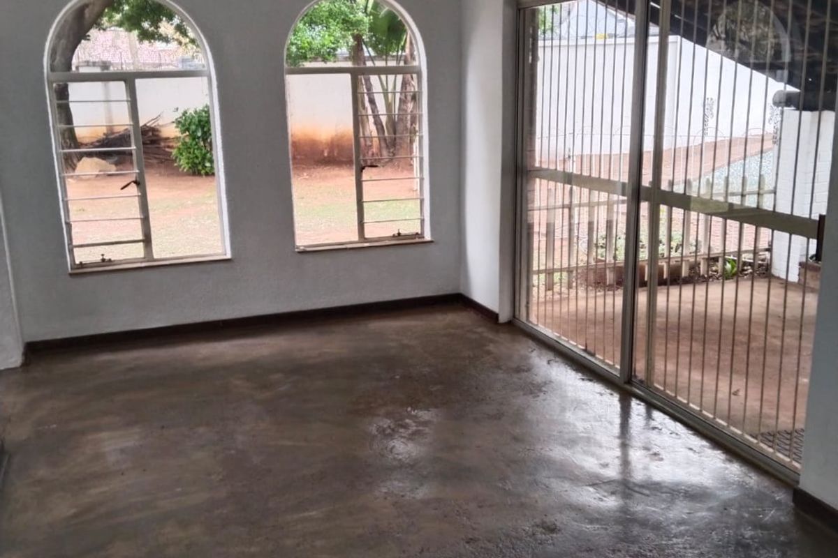 An empty living area featuring exposed timber ceiling beams, arched windows, and sliding glass doors with security bars, opening onto an outdoor space.