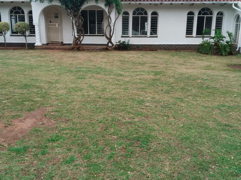 Rear view of a single-story house featuring a terracotta tiled roof, arched windows, and a spacious lawn area.