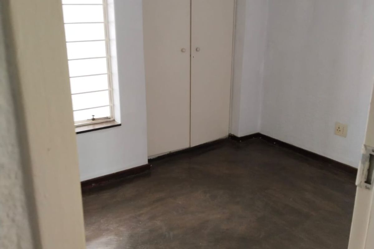 An empty bedroom featuring built-in cupboards, a window with security bars, and dark concrete flooring.