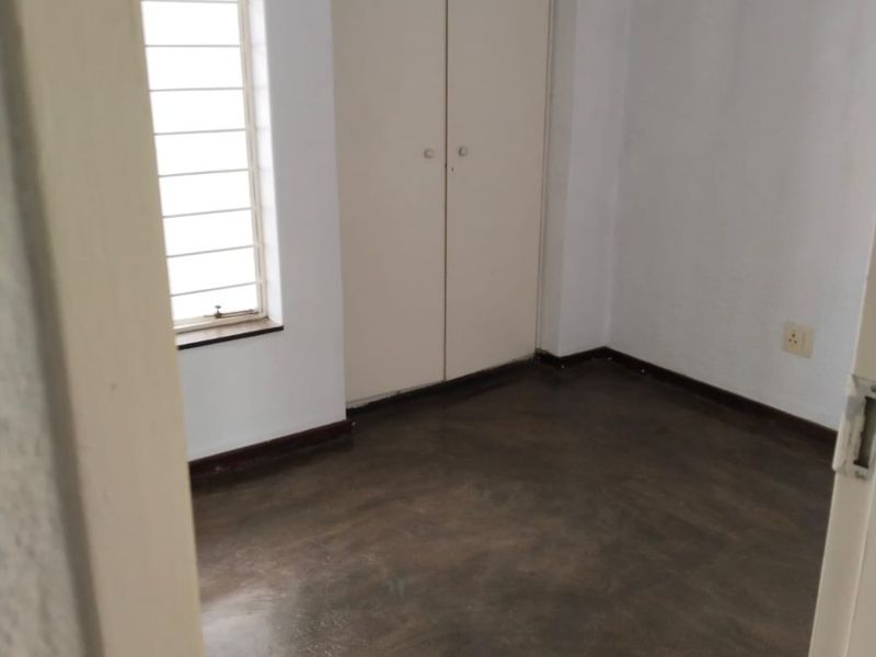 An empty bedroom featuring built-in cupboards, a window with security bars, and dark concrete flooring.