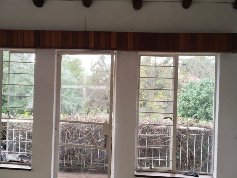 An empty living area featuring exposed timber ceiling beams, security bars on windows, and a security door leading to the exterior.