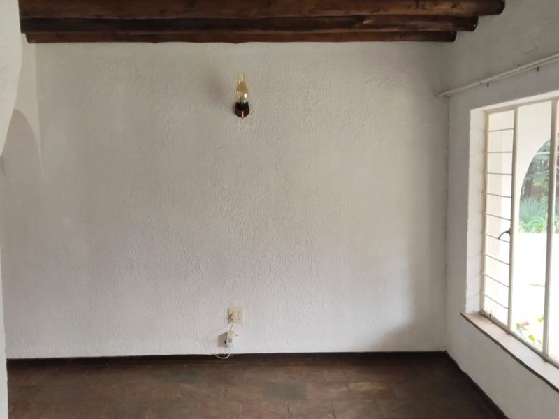 An empty living area featuring rustic exposed timber ceiling beams, terracotta tile flooring, and a large steel-framed window.