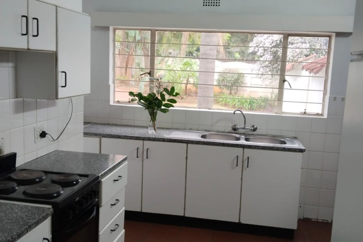 A functional kitchen featuring white cabinetry, a double basin sink, electric stove, and vaulted ceilings with exposed timber beams, overlooking the garden.