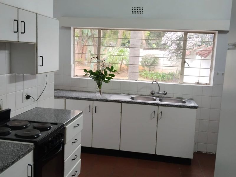 A functional kitchen featuring white cabinetry, a double basin sink, electric stove, and vaulted ceilings with exposed timber beams, overlooking the garden.