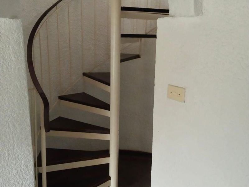 A functional spiral staircase featuring dark wood treads and a metal frame, set within a textured white arched entryway.