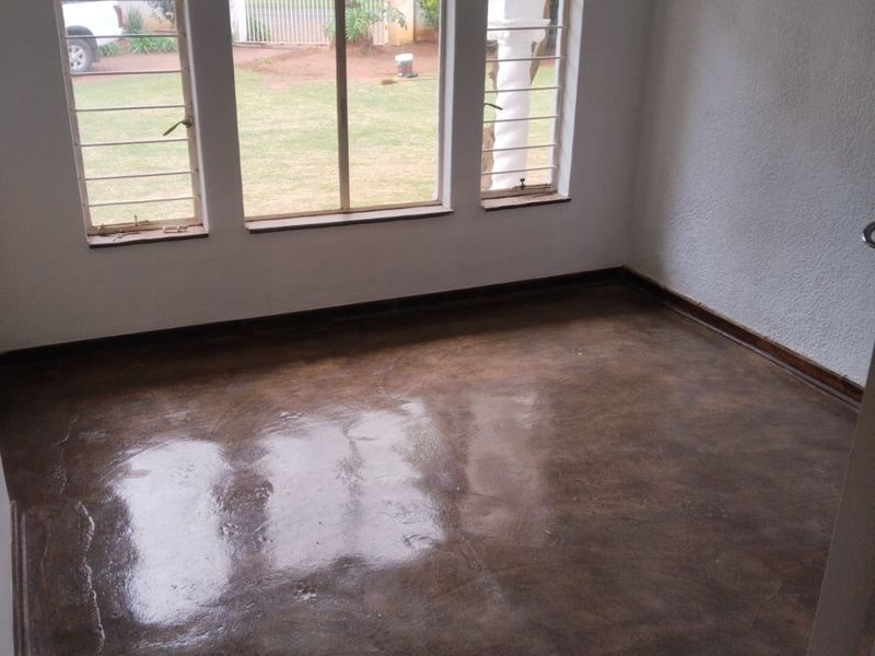 An empty living room featuring polished concrete flooring and three large arched windows with security bars, offering a view of the front garden.