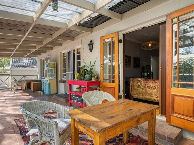 A covered outdoor patio area featuring tiled flooring, a translucent roof structure, and timber-framed doors providing access to the interior living space.