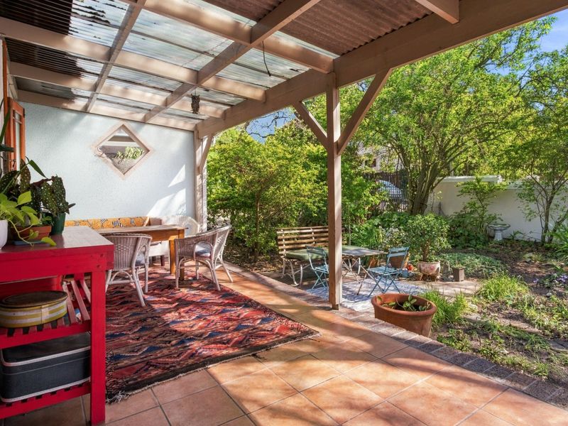 A covered outdoor patio featuring a timber pergola with translucent roofing and tiled flooring, overlooking a private garden area.