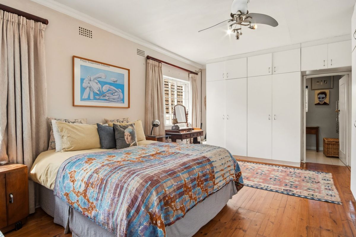 Spacious bedroom featuring polished timber flooring, extensive built-in storage cupboards, and a ceiling fan, offering a comfortable and functional living space.