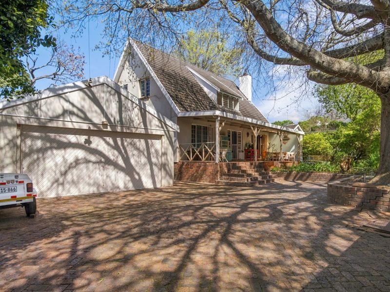 Front view of a charming house featuring a brick-paved driveway, double garage, and a covered veranda with brick steps.