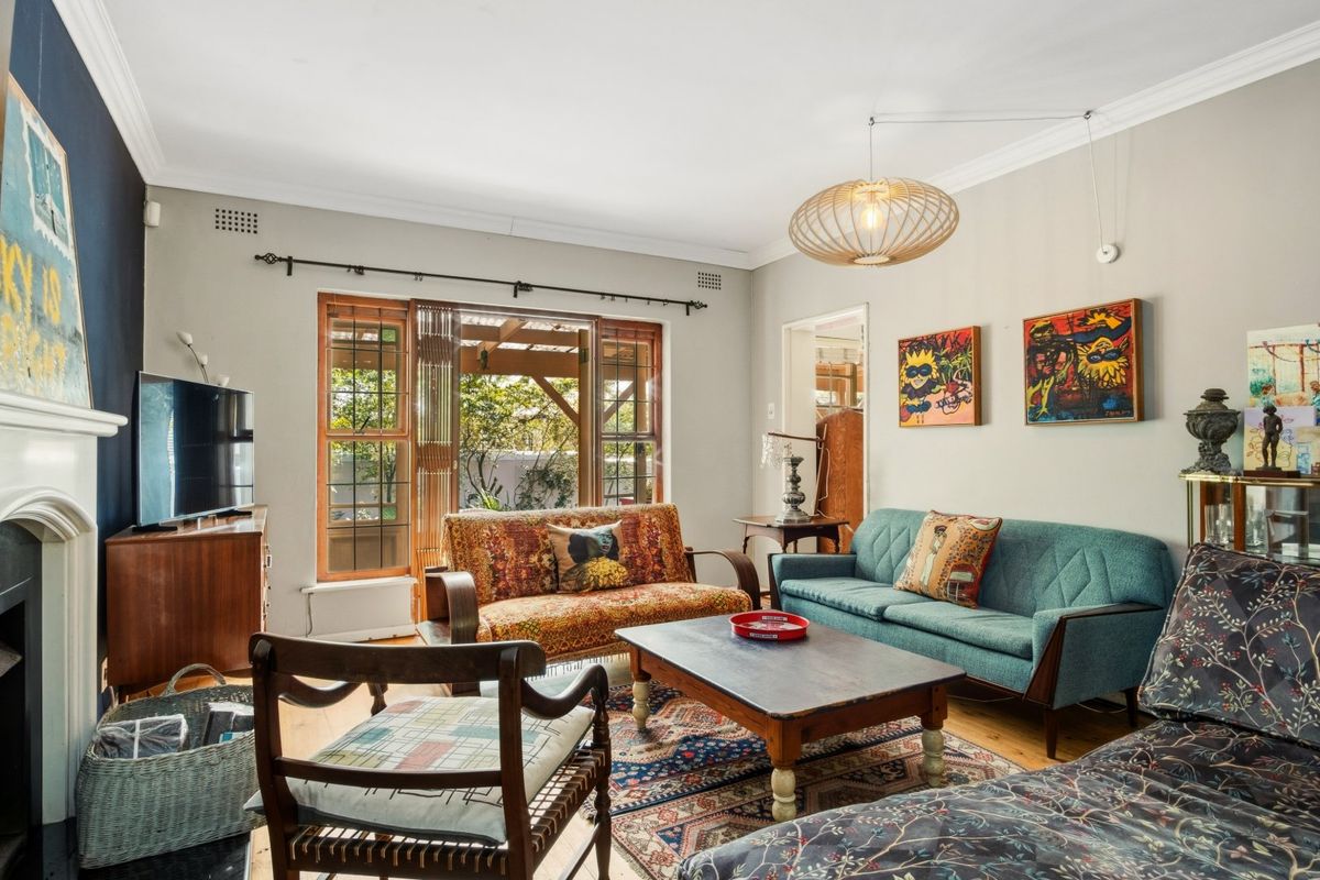 A well-maintained living room featuring hardwood flooring, a fireplace, and large timber-framed windows that provide natural light and access to the outdoor area.
