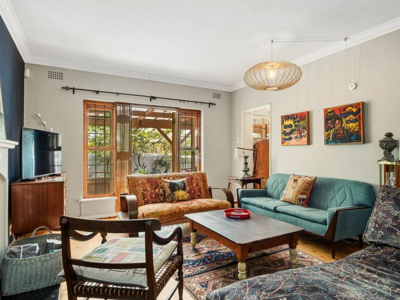 A well-maintained living room featuring hardwood flooring, a fireplace, and large timber-framed windows that provide natural light and access to the outdoor area.