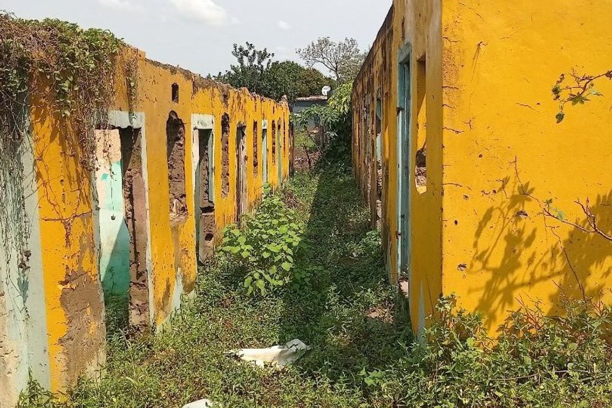 A severely dilapidated structure showing extensive structural damage, missing roof sections, and significant overgrowth, indicating a property in need of major redevelopment.