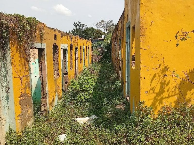 A severely dilapidated structure showing extensive structural damage, missing roof sections, and significant overgrowth, indicating a property in need of major redevelopment.