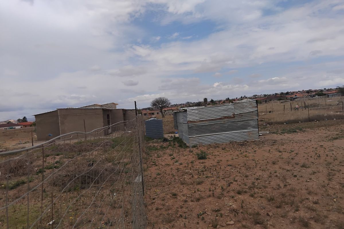 Vacant residential land featuring wire fencing, a water storage tank, and a small corrugated metal structure on the property.