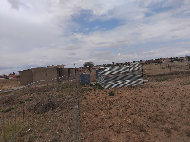 Vacant residential land featuring wire fencing, a water storage tank, and a small corrugated metal structure on the property.