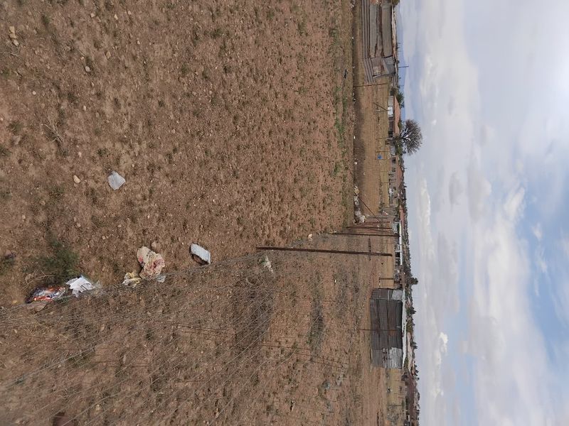 A vacant residential plot featuring wire mesh perimeter fencing and open, undeveloped land.