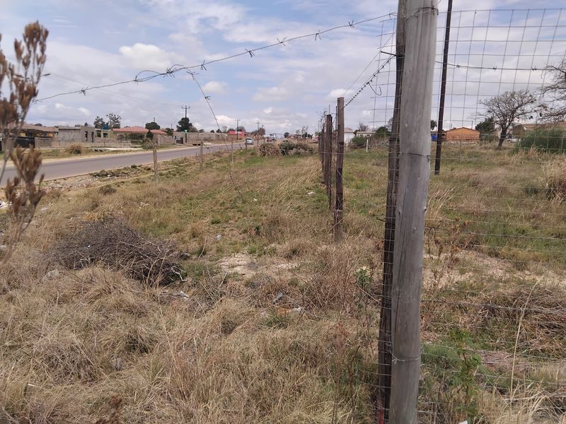 A view of the vacant residential plot showing the street frontage and existing wire perimeter fencing.