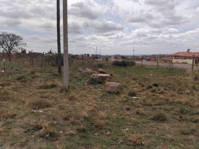 A view of a vacant residential plot featuring natural grass, a utility pole, and perimeter wire fencing.