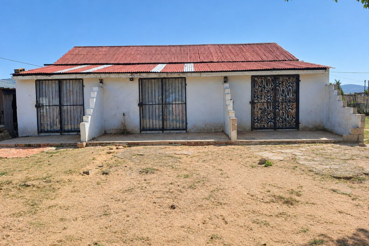 Rear view of a single-story dwelling featuring a corrugated metal roof, tiled patio area, and multiple security-gated entrances.