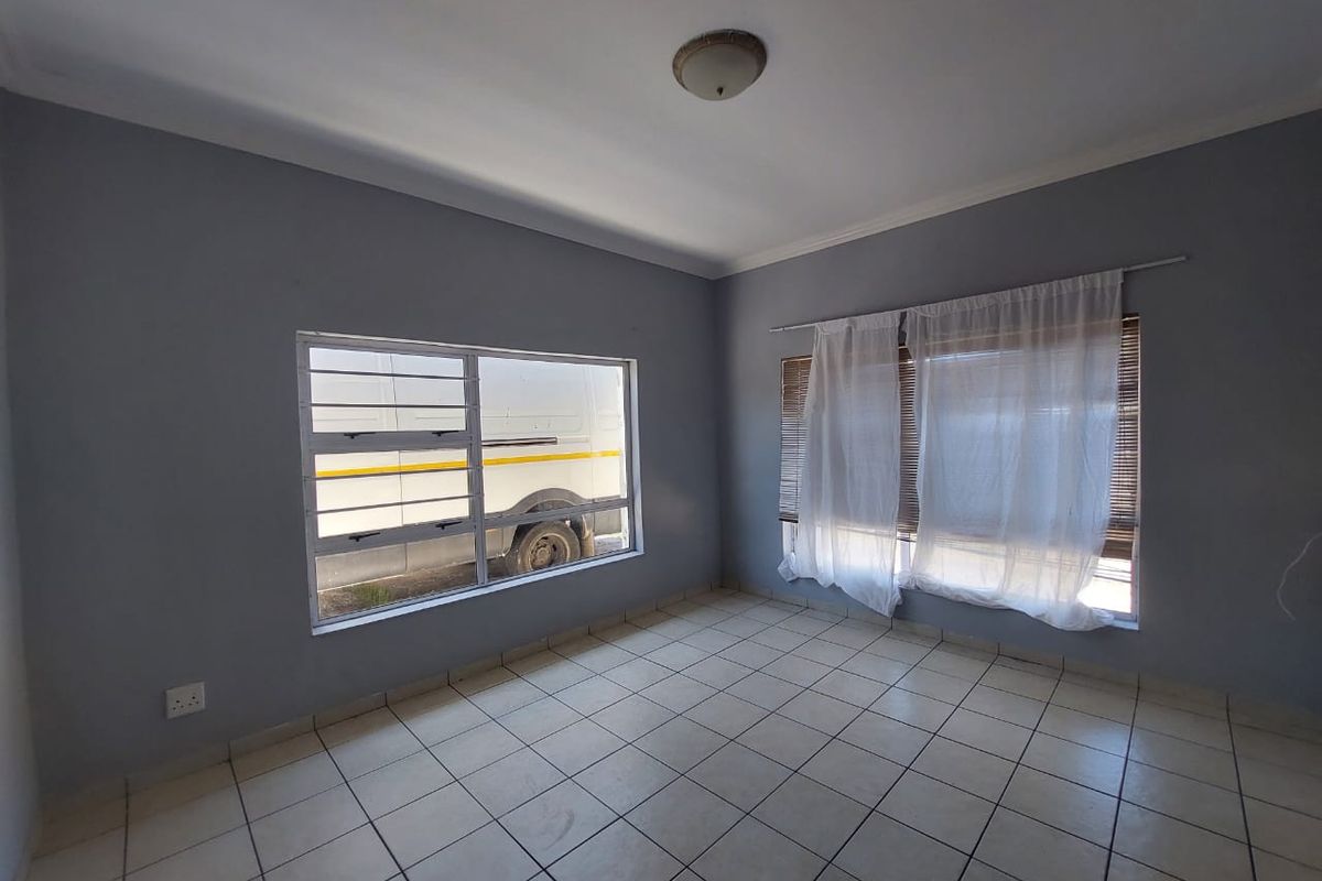 An empty bedroom featuring tiled flooring, security bars on the windows, and neutral grey walls, offering a blank canvas for personalization.