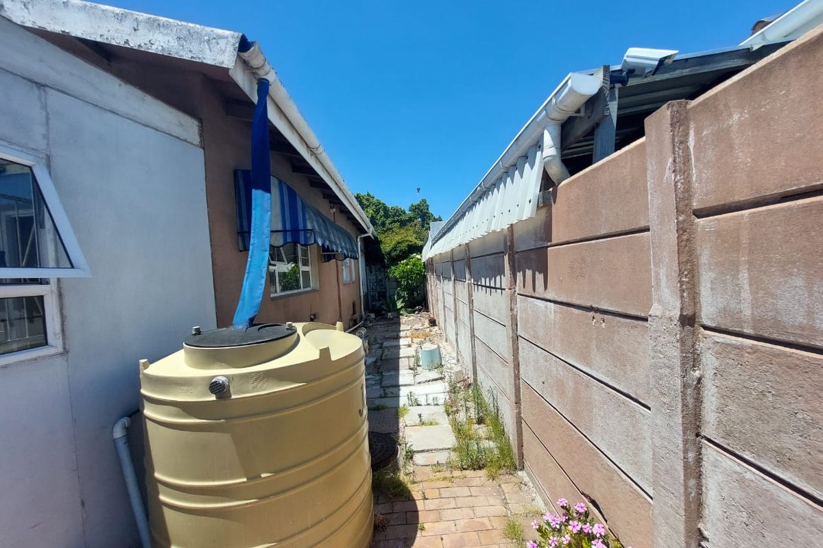 A narrow side passage featuring a water storage tank, precast concrete boundary wall, and paved walkway with some maintenance required on gutters and paving.