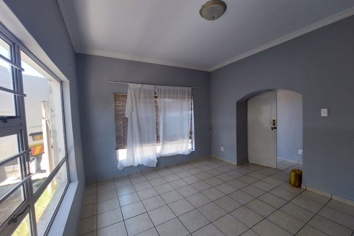 An empty living room featuring tiled flooring, an arched doorway, and neutral grey walls, offering a blank canvas for interior design.