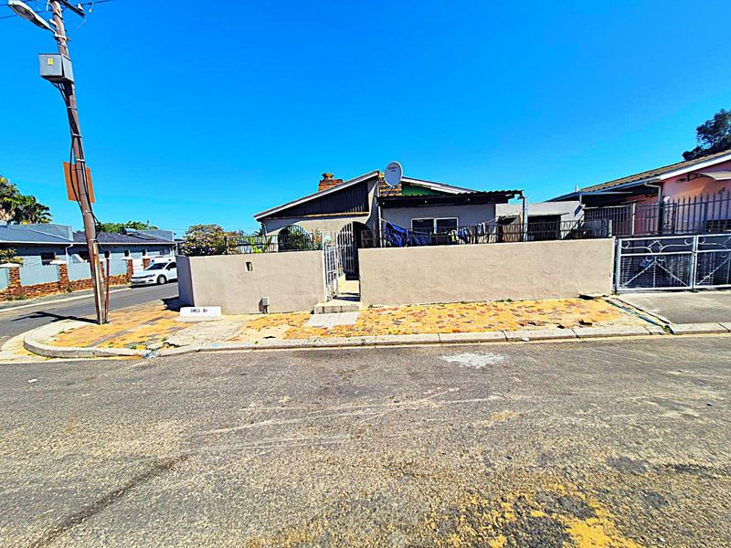 Street-facing view of a single-story house featuring a boundary wall, paved front area, and metal security gate access.