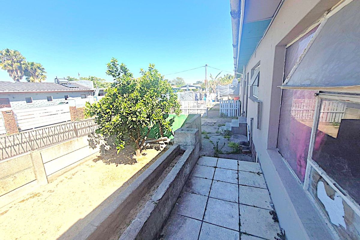 Rear exterior view showing a paved patio area, concrete planter box, and precast boundary wall with signs of weathering and maintenance requirements.