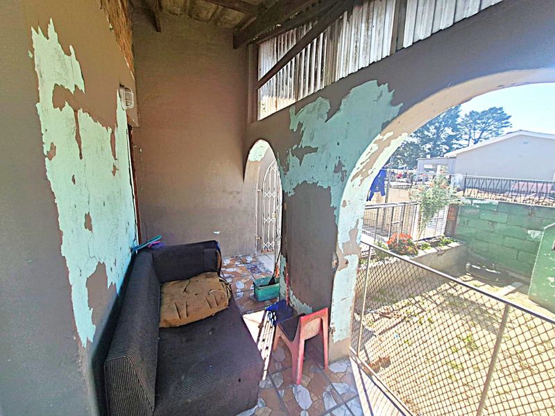 A covered patio area featuring arched architectural details, tiled flooring, and a security gate, currently requiring significant maintenance to the wall finishes.