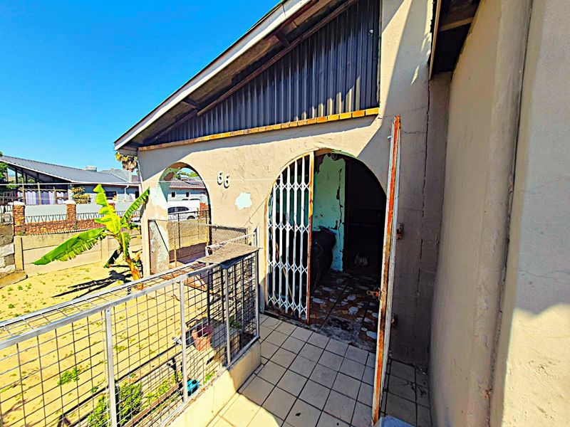 Front entrance area featuring a security gate, tiled patio, and plastered masonry walls showing signs of significant wear and weathering.