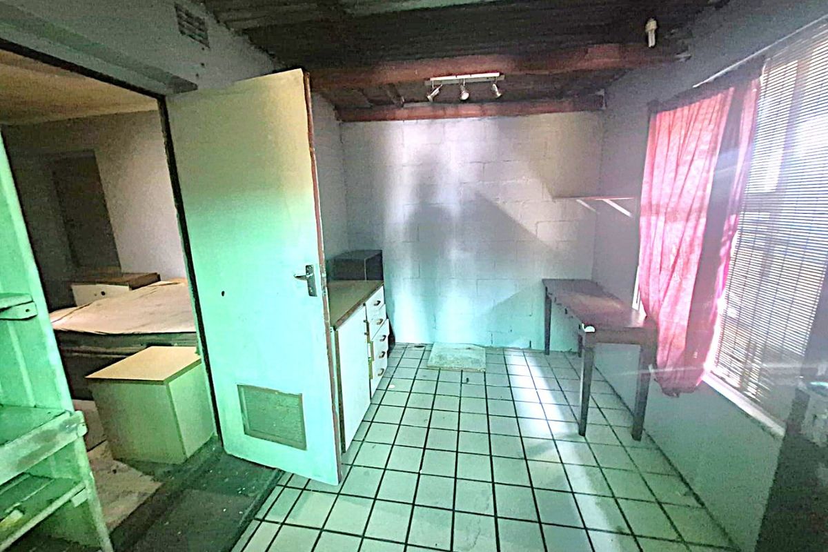 A basic kitchen area featuring tiled flooring, exposed timber ceiling beams, and built-in cabinetry, requiring significant renovation and cosmetic updates.